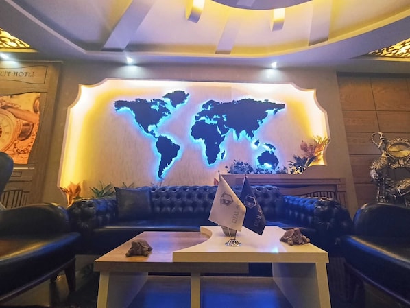 Um hall com um mural de um mapa-múndi, um sofá, uma mesa com uma bandeira e um relógio.
