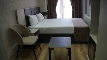 A hotel room with a bed, a chair, a small table, and a window with curtains.