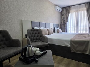 Una habitación de hotel con una cama, dos sillones, una mesita de centro con hervidor y tazas, y una ventana con cortinas.