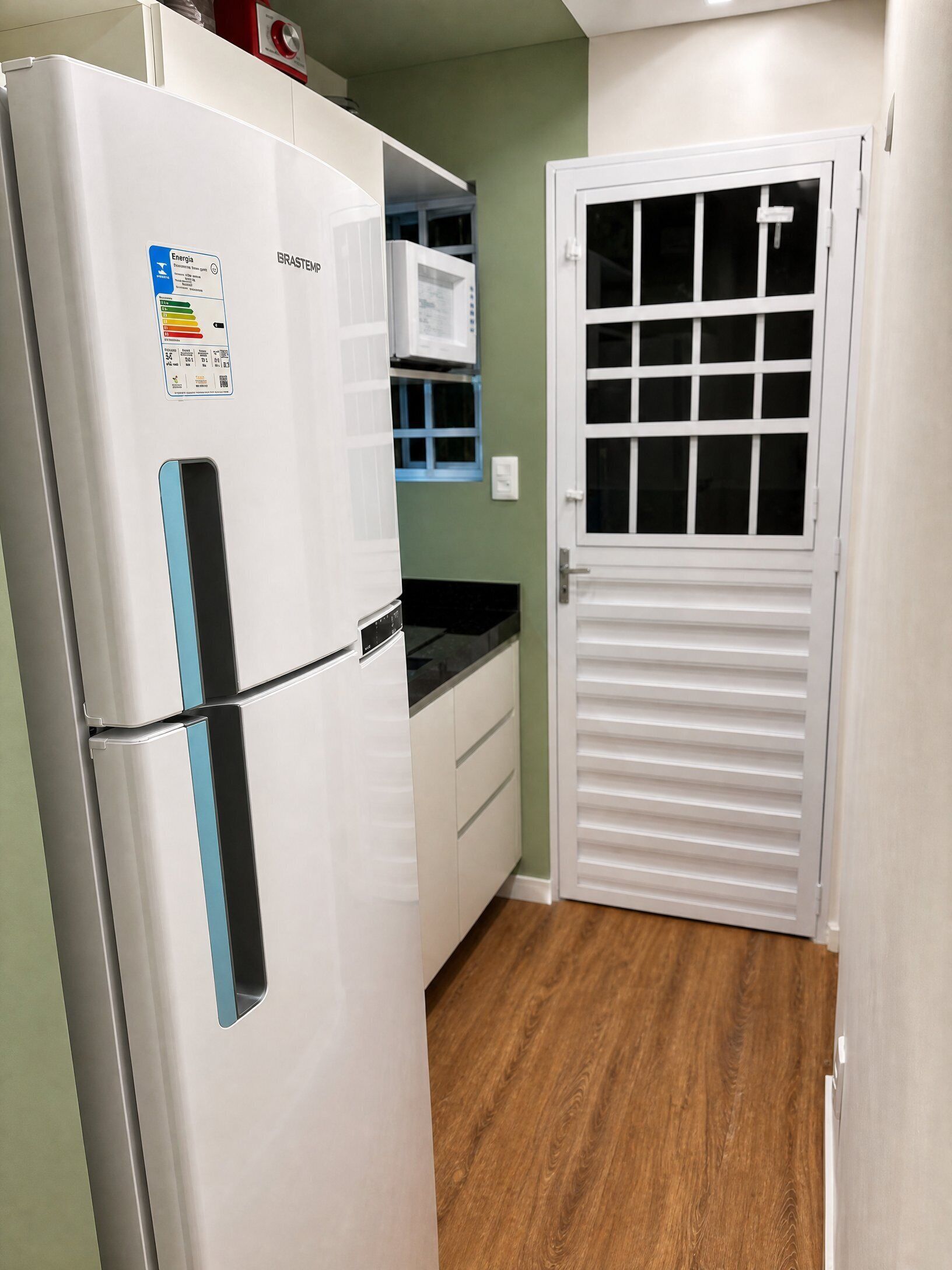 Eine kleine Küche mit einem weißen Kühlschrank, einer Mikrowelle und einer weißen Tür mit Fenster.