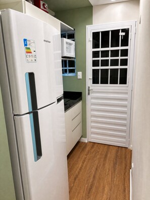 A compact kitchen with a white refrigerator, a microwave, and a white door with a window. - 2-bedroom apartment in downtown Recife - 120m from UNICAP, garage and WiFi. (Recife)