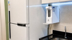 Ett kök med ett vitt kylskåp, en vattenautomat och en svart diskho inbyggd i bänkskivan.