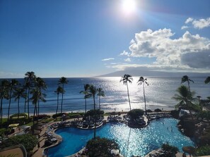 Ein Poolbereich einer Ferienanlage mit Palmen, blauem Himmel und Blick auf den Ozean.