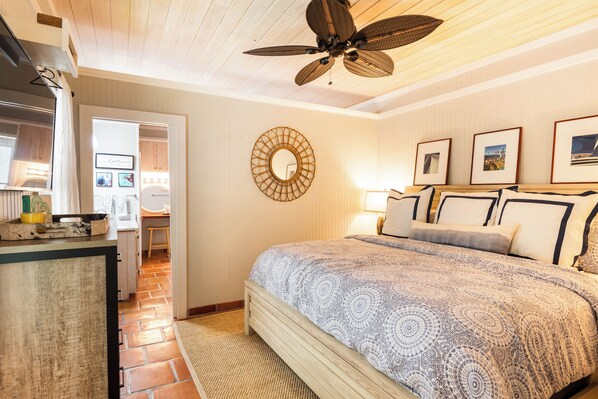 A bedroom with a bed, a ceiling fan, a wall-mounted mirror, and framed pictures.