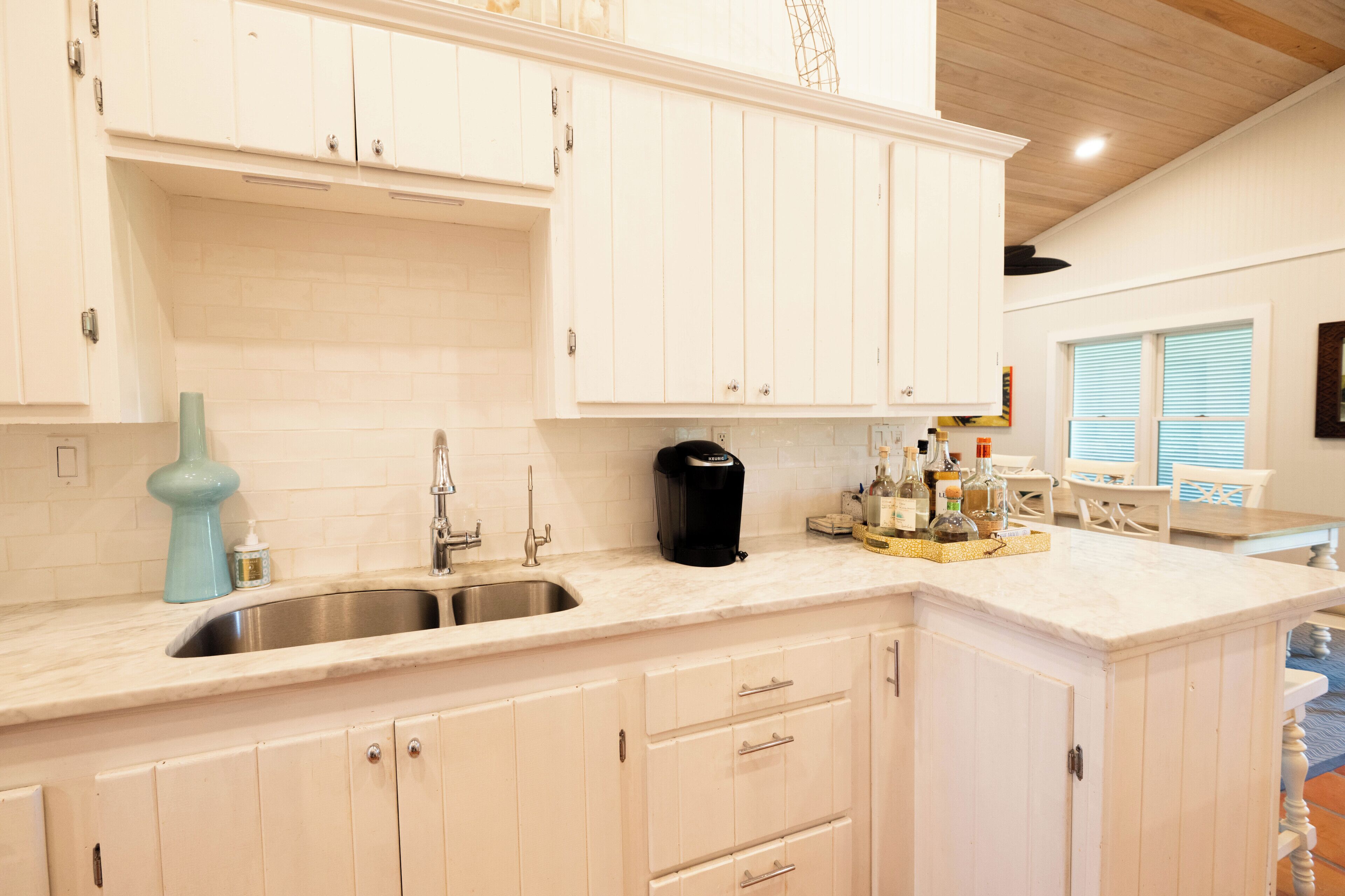 A kitchen with white cabinets, a sink, a coffee maker, and a dining area with a table and chairs.