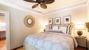 A bedroom with a large bed, a ceiling fan, a round mirror, and framed pictures on the wall.