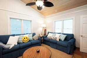 A living room with two blue sofas, a wooden coffee table, and a ceiling fan.