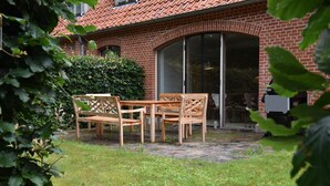 Ein Ziegelhaus mit Terrasse, Holzmöbeln und einer großen Schiebeglastür.
