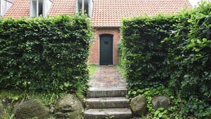 Ein Backsteinhaus mit rotem Ziegeldach, einer schwarzen Tür und einer schmalen Steintreppe, die zum Eingang führt.