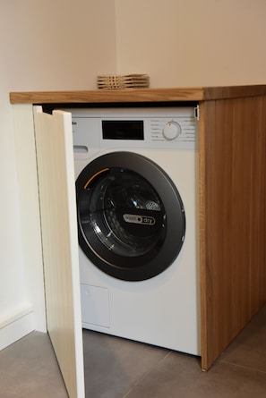 A compact, modern washing machine with a control panel and a wooden shelf above it. - Exclusive "Steuerbord" vacation rental with private boat access and dock (Boren)