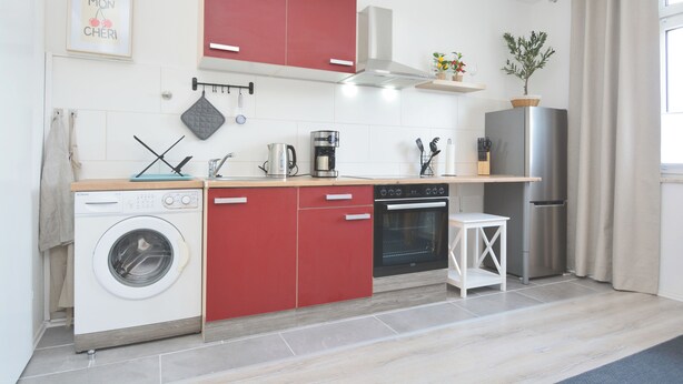 Een kleine keuken met een wasmachine, een koffiezetapparaat, een kookplaat en een koelkast.