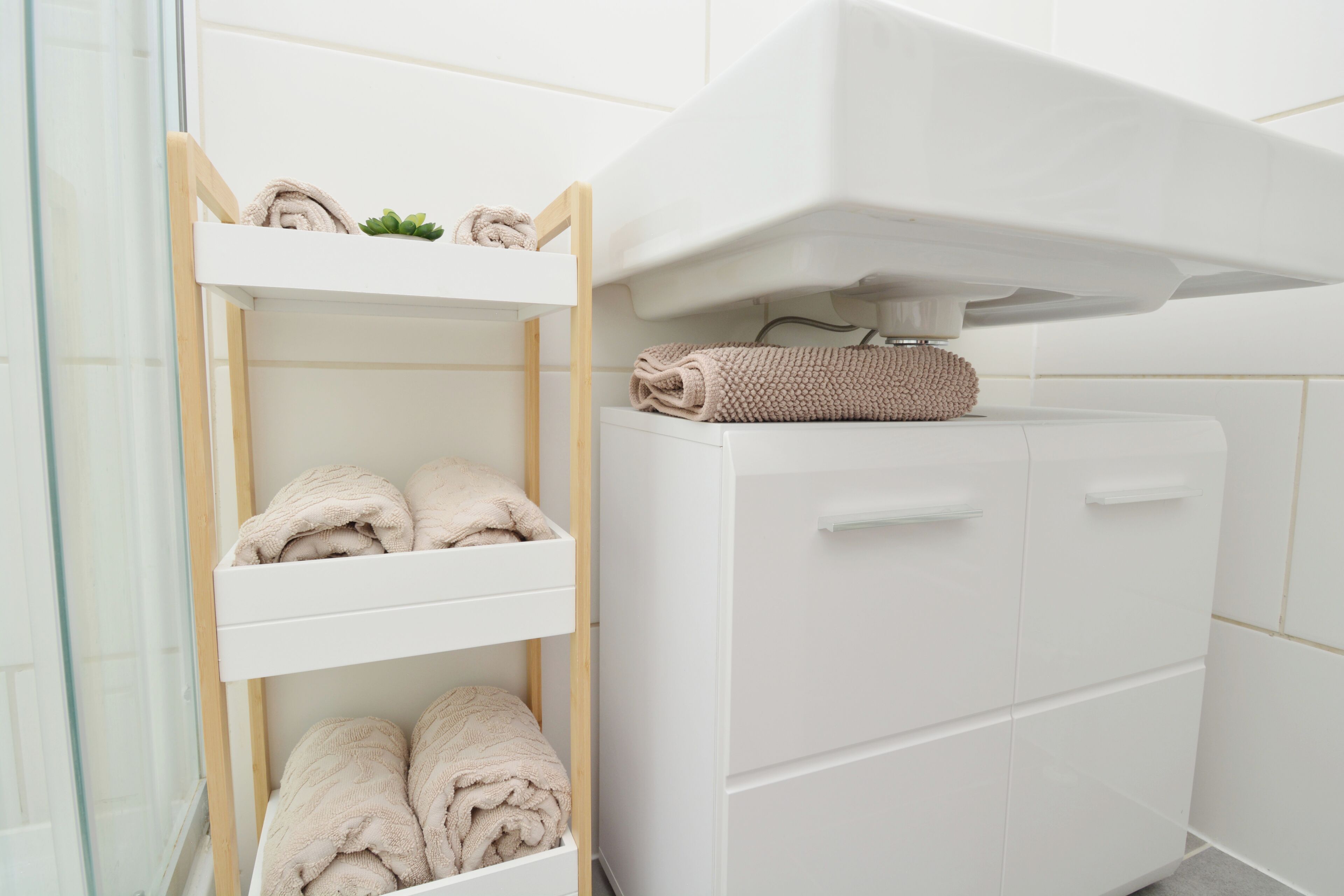 Une salle de bain avec un meuble-lavabo blanc, une étagère en bois où sont posées des serviettes et une cabine de douche en verre.