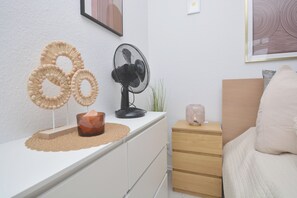 A bedroom with a white dresser, a bedside table with a lamp, a bed with a white pillow, and wall art.
