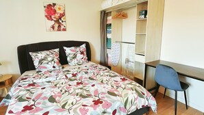 A bedroom with a bed, a desk, a chair, a wardrobe, and a painting on the wall.