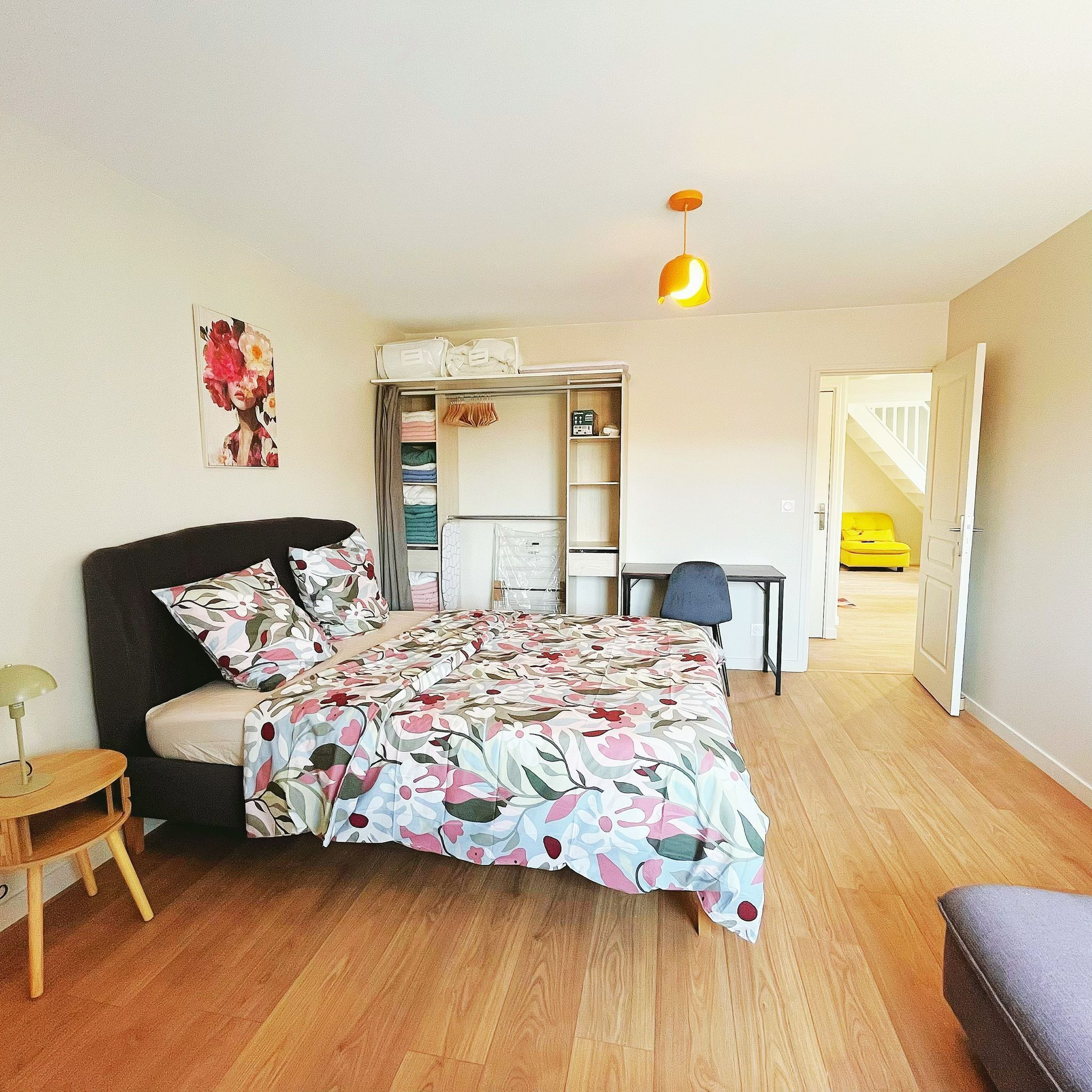 A bedroom with a bed, a desk, a chair, a wardrobe, and a door leading to another room.