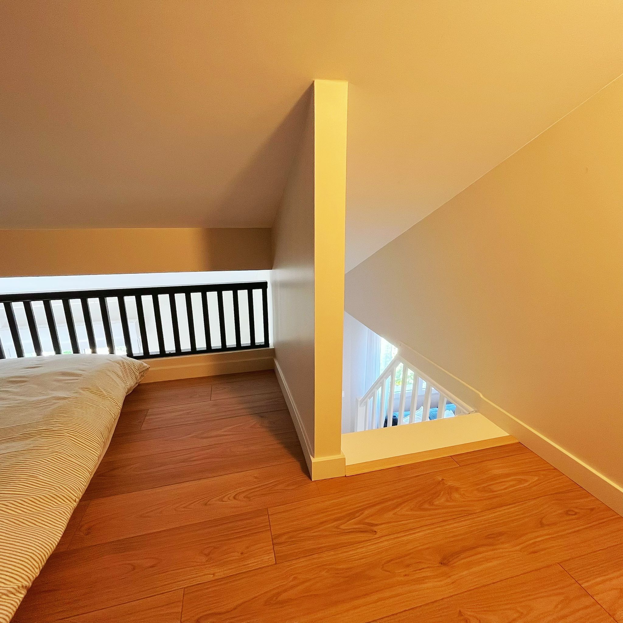 Une pièce avec un plafond en pente, un plancher en bois, une rambarde blanche et un lit recouvert d’une couvre-lit à motifs.