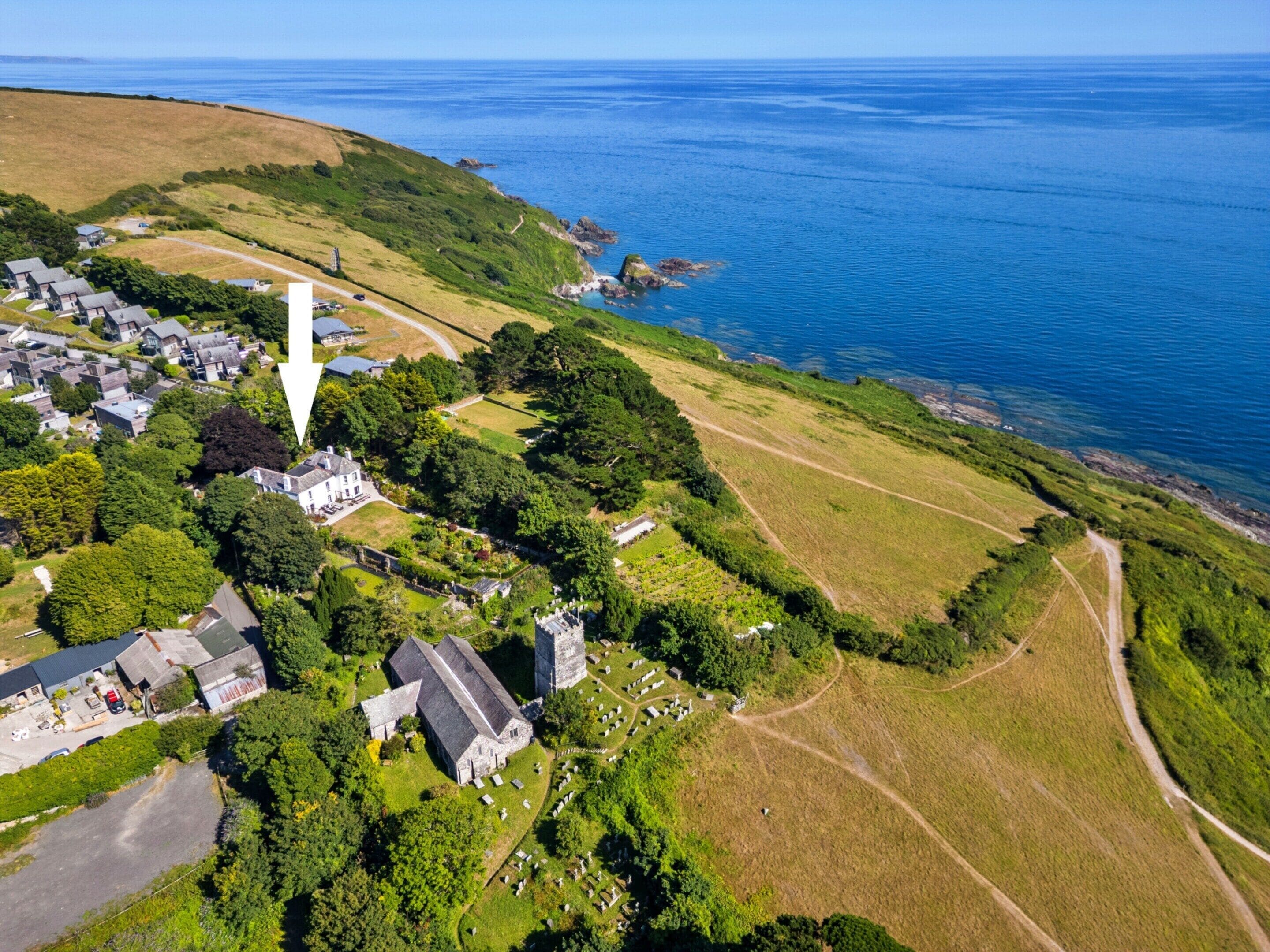 An aerial view of a coastal village with a prominent church, a cemetery, and a sea view.