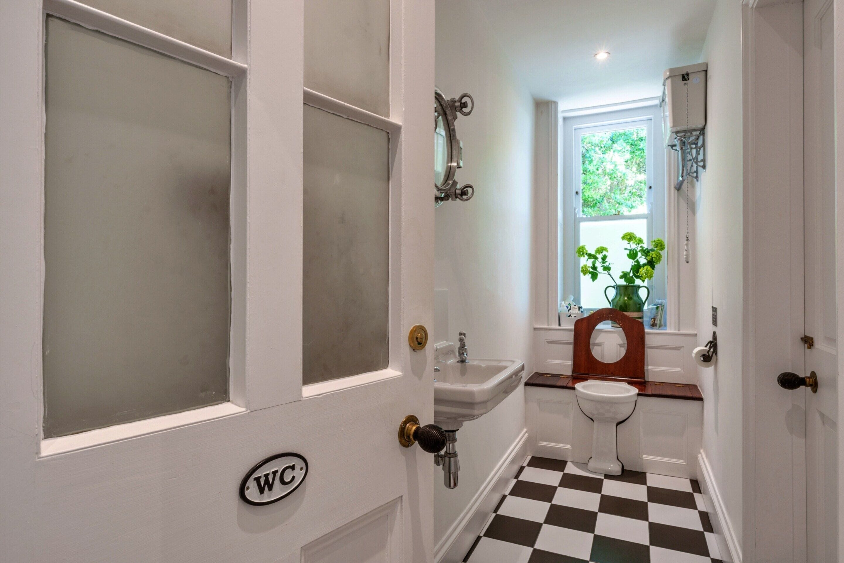 Une salle de bain avec un carrelage à motifs géométriques, un lavabo, des toilettes et une fenêtre donnant sur un paysage verdoyant.