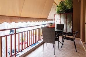 Een balkon met een tafel en stoelen, een rode leuning en uitzicht op geparkeerde auto's.