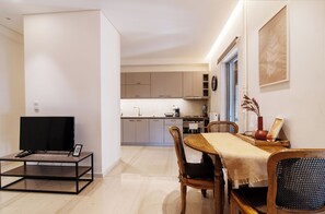 Eine moderne Küche mit grauen Schränken, ein Essbereich mit Holztisch und Stühlen sowie ein Fernseher auf einem Schrank.