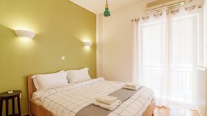 A neatly made bed with a checkered bedspread and pillows, a bedside table with a lamp, and a window with curtains.