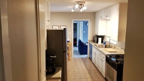 Cocina pequeña con refrigerador, estufa y microondas. Se ve un comedor con una mesa y sillas al fondo.