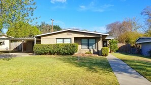 A single-story house with a front porch, a covered garage, and a well-maintained lawn. - Spacious 3bedroom house in the heart of San Antonio with Pool/hottub and Game Rm (San Antonio)