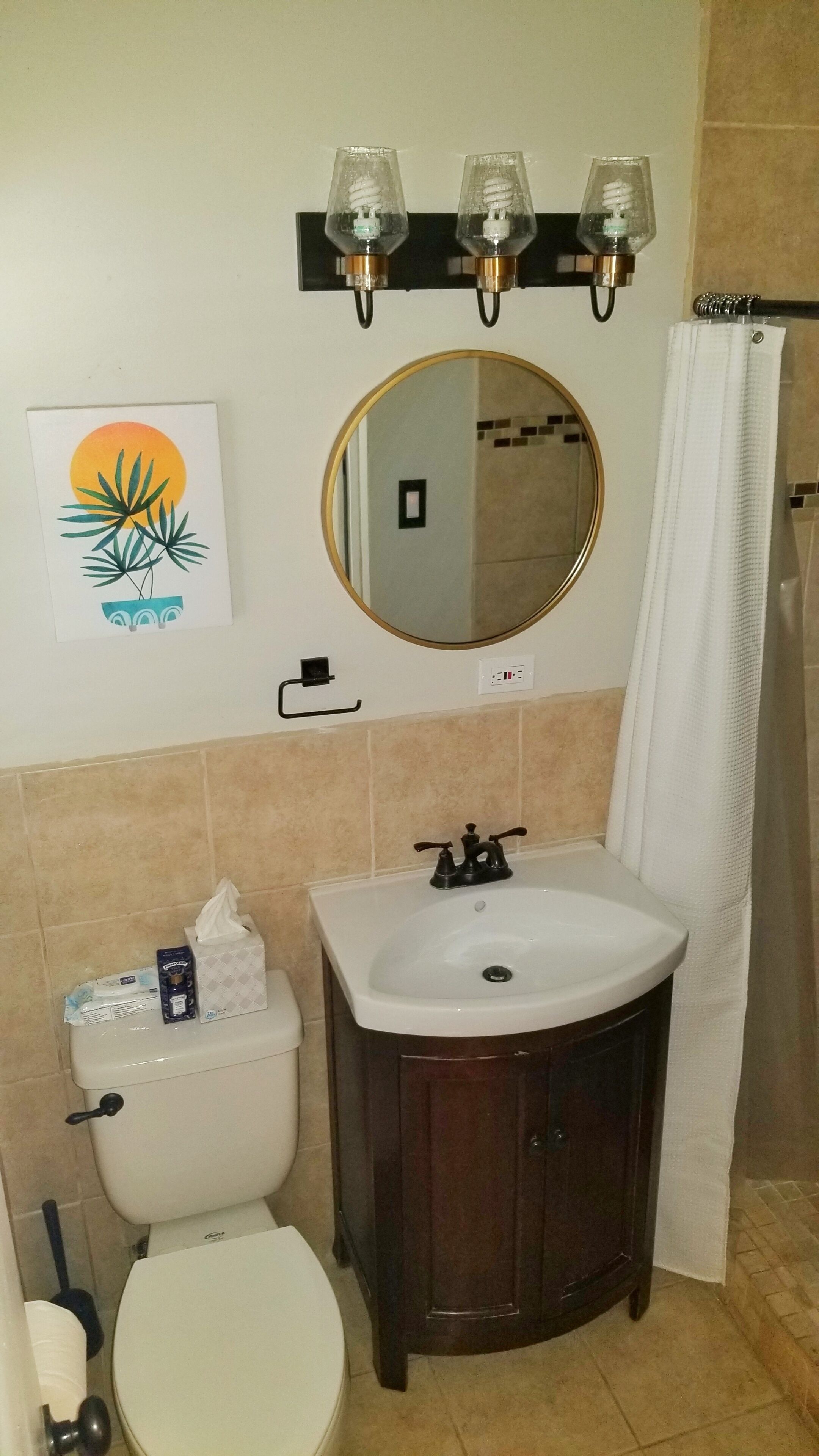 Une salle de bain équipée de toilettes, d’un lavabo, d’un miroir et de trois appliques murales.