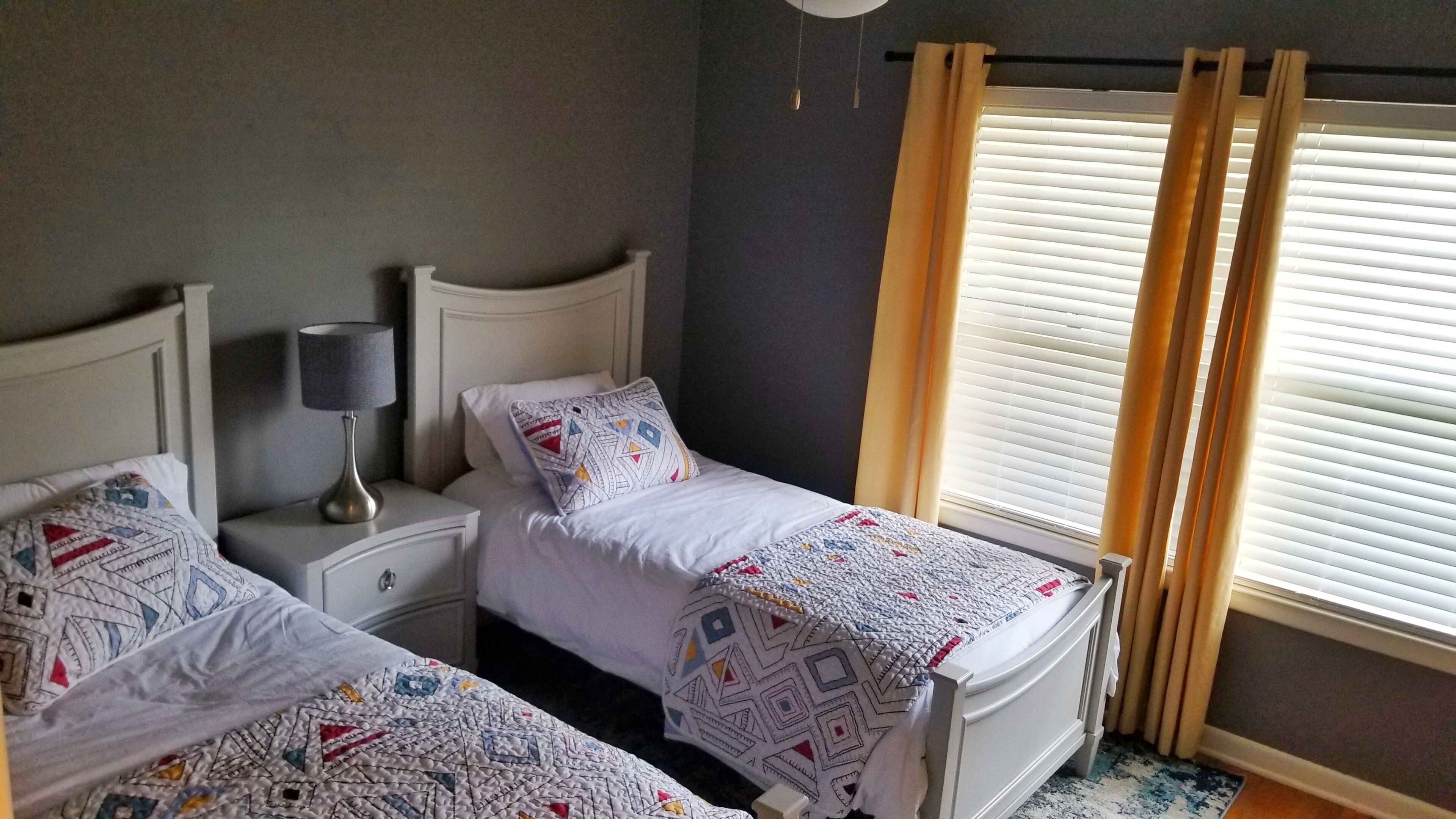 Une chambre avec deux lits, une table de chevet avec une lampe et une fenêtre avec des stores.