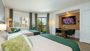 Ein Hotelzimmer mit zwei Betten, einem Balkon, einem Essbereich und einem Fernseher, der Feuerwerkskörper zeigt.