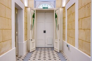 A hallway with a patterned floor, a white door with a green exit sign, and a brick wall. - Charming 1BR Maltese Maisonette w/ Terrace, Luqa (Ħal Luqa)