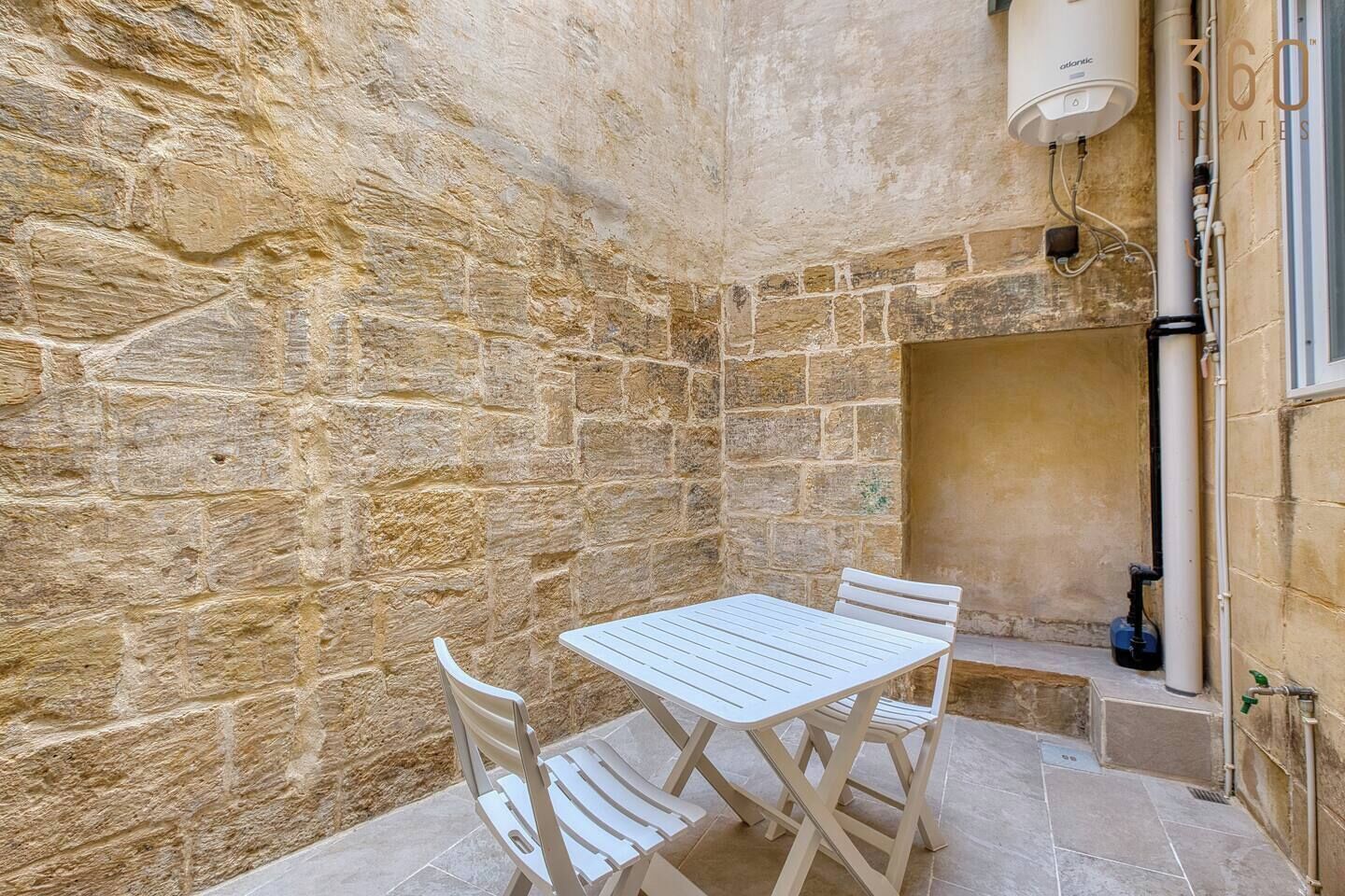 A stone-walled room with a white table and chairs, a water heater, and a window.