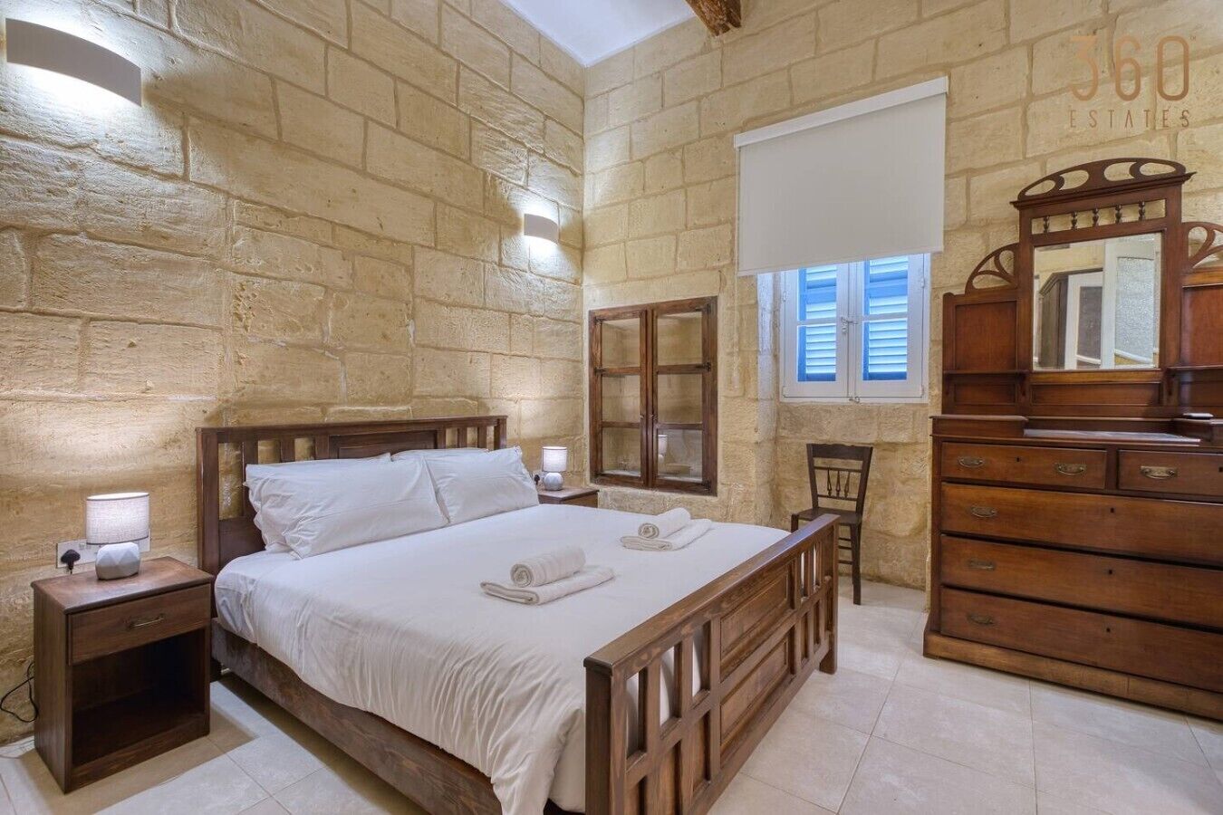 A bedroom with a wooden bed, nightstands, a dresser, a mirror, and a stone wall.