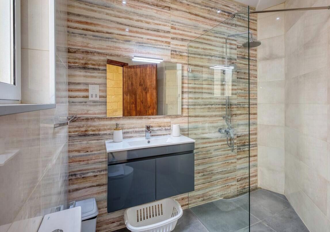 A modern bathroom with a marble wall, a glass shower enclosure, and a sink with a dark cabinet.