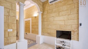 A room with a fireplace, a television on a stand, and a brick wall. - Charming 1BR Maltese Maisonette w/ Terrace, Luqa (Ħal Luqa)
