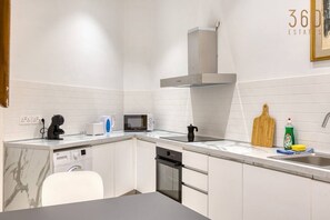 A modern kitchen with white cabinetry, a built-in microwave, a coffee maker, and a sink with a cutting board and dish soap. - Charming 1BR Maltese Maisonette w/ Terrace, Luqa (Ħal Luqa)