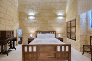 Ein Schlafzimmer mit einem hölzernen Bett, zwei Nachttischen mit Lampen, einem Schreibtisch mit einem Computer und einer Steinwand.