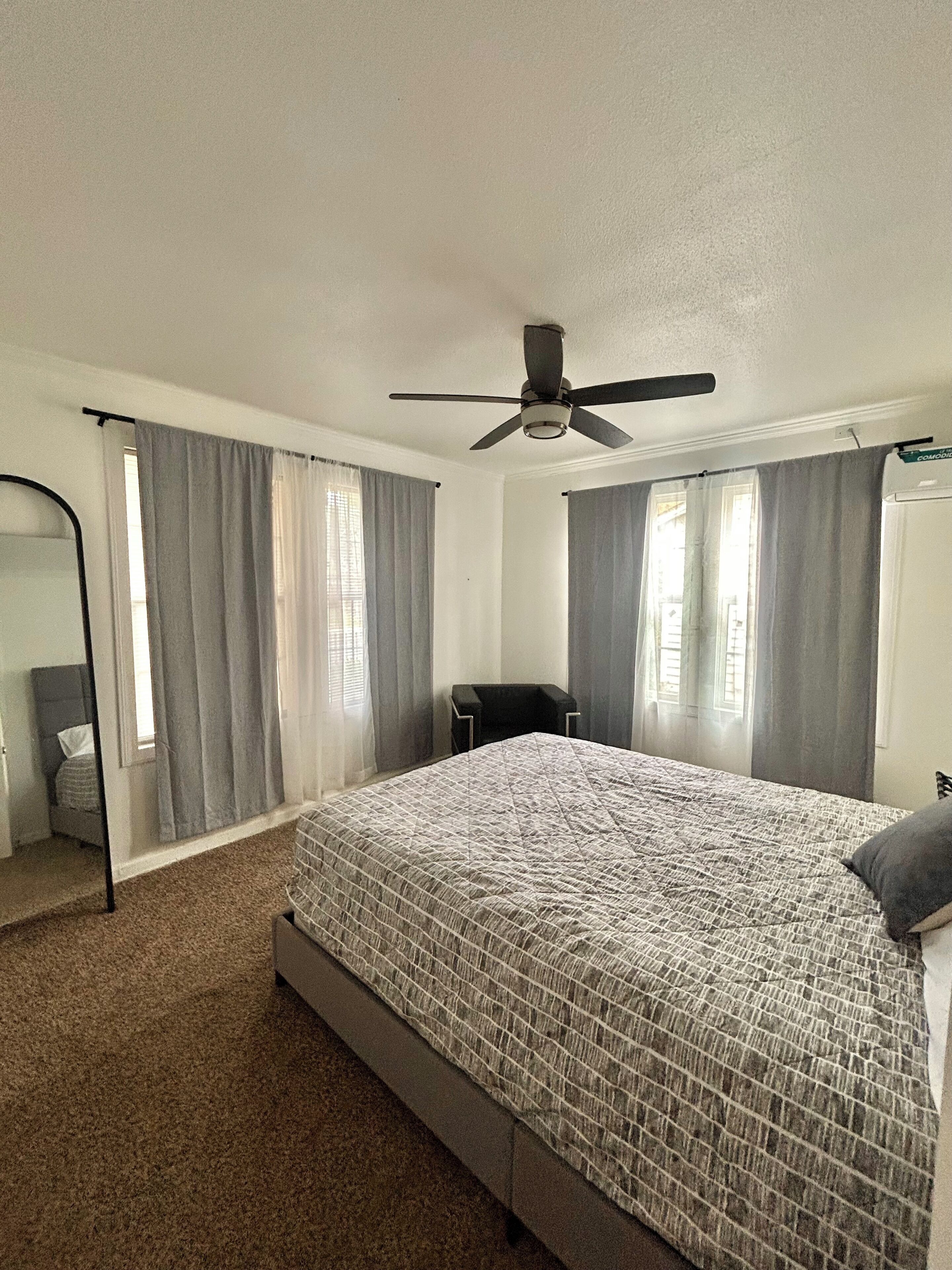 Ein Schlafzimmer mit einem Bett, einem Deckenventilator, einem Sessel und einem Schreibtisch.