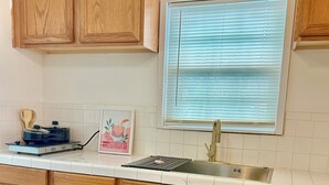A kitchen with wooden cabinets, a stainless steel sink, and a window with blinds. - Cozy 2-bedroom house in delightful San Antonio with AC (San Antonio)