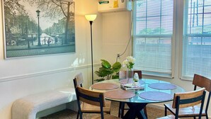 A dining area with a round table, four chairs, a bench, a wall-mounted air conditioner, a floor lamp, and a large framed picture. - Cozy 2-bedroom house in delightful San Antonio with AC (San Antonio)