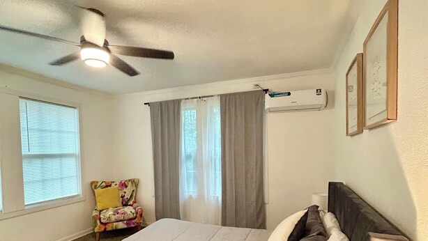 A bedroom with a bed, a ceiling fan, a window with blinds, a chair, and a wall-mounted air conditioner. - Cozy 2-bedroom house in delightful San Antonio with AC (San Antonio)