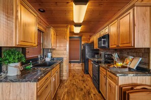 A kitchen with wooden cabinets, a black refrigerator, a microwave, and a granite countertop. - Panoramic Views|Hot Tub|Game Room|Resort Pool (Sevierville)