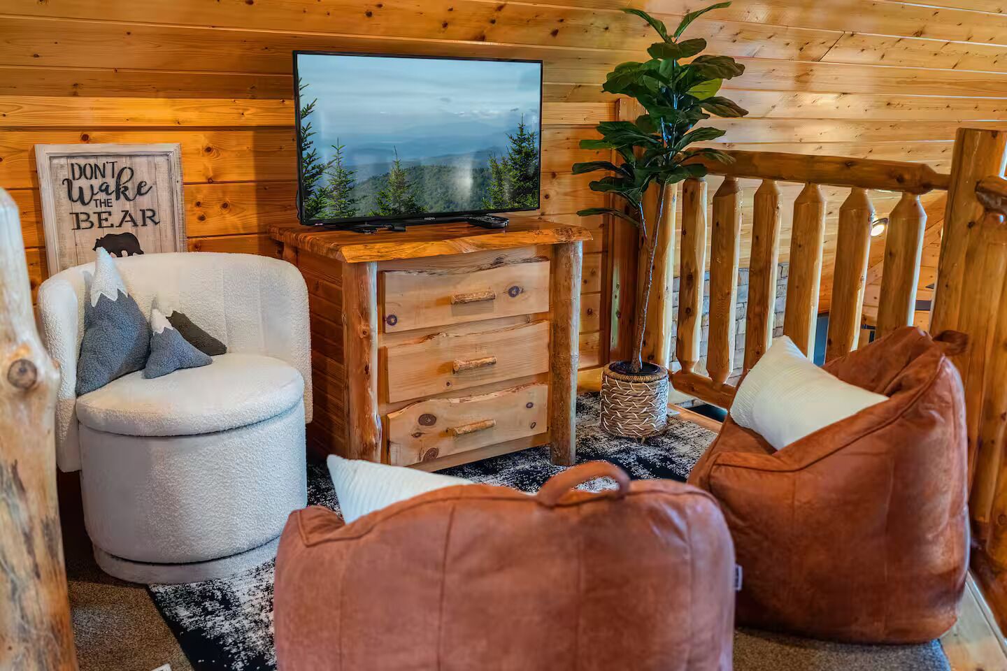 A cozy cabin interior with a television, a sofa, a loveseat, and a wooden dresser.