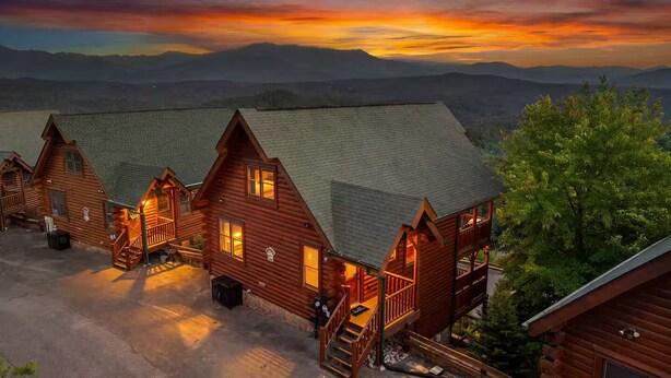 A log cabin hotel with multiple rooms, a covered outdoor area, and a scenic mountain backdrop. - Panoramic Views|Hot Tub|Game Room|Resort Pool (Sevierville)