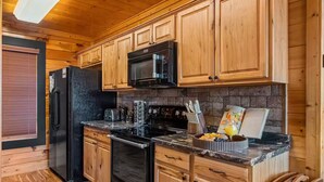 A kitchen with wooden cabinets, a black refrigerator, a microwave, a stove, and a sink. - Panoramic Views|Hot Tub|Game Room|Resort Pool (Sevierville)