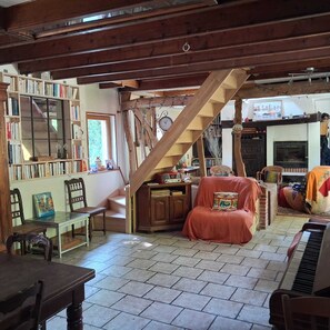 A cozy living room with a staircase, a fireplace, a piano, and a bookshelf. - Country house just 5 minutes from the ocean! (Longueil)