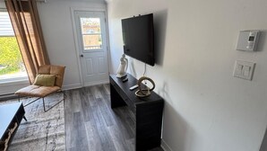 A modern living room with a flat-screen TV, a black console table, a leather chair, and a grey wooden floor. - Elegant and cozy  5 1/2 appartement with pool (Longueuil)