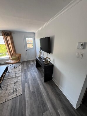 A modern living room with a flat-screen TV, a black console table, a leather chair, and a grey wooden floor. - Elegant and cozy  5 1/2 appartement with pool (Longueuil)