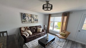 A living room with a brown leather sofa, a coffee table, a rug, and a painting on the wall. - Elegant and cozy  5 1/2 appartement with pool (Longueuil)