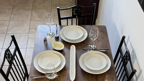 A dining table set with plates, glasses, and cutlery, surrounded by black chairs. - Elegant and cozy  5 1/2 appartement with pool (Longueuil)